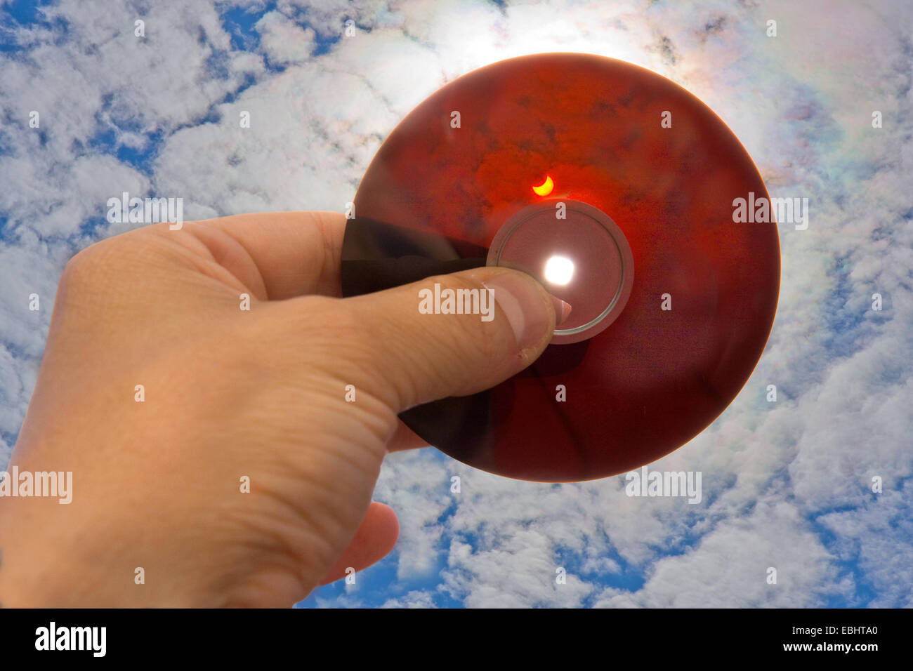Una mano che tiene la parte interna di un disco floppy verso il sole per proteggere gli occhi quando si guarda una parziale eclissi solare. Foto Stock