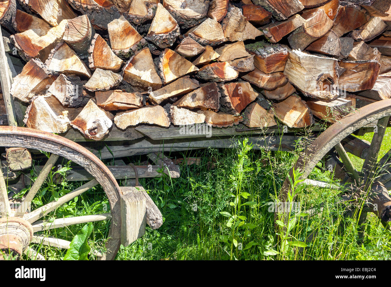 Tronchi di legna da ardere impilati in pile all'esterno di un cottage, vecchio carrello in legno, giardino in legno carretto in legno tronchi impilati Foto Stock