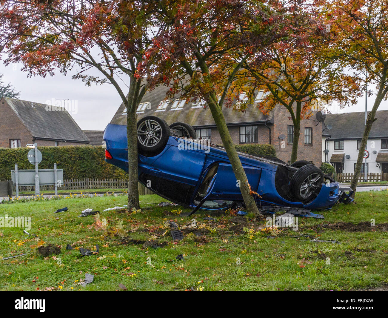 Insolito incidente automobilistico, raffiguranti blu berlina sportiva veicolo sul suo tetto, tra gli alberi su una rotatoria isola Foto Stock