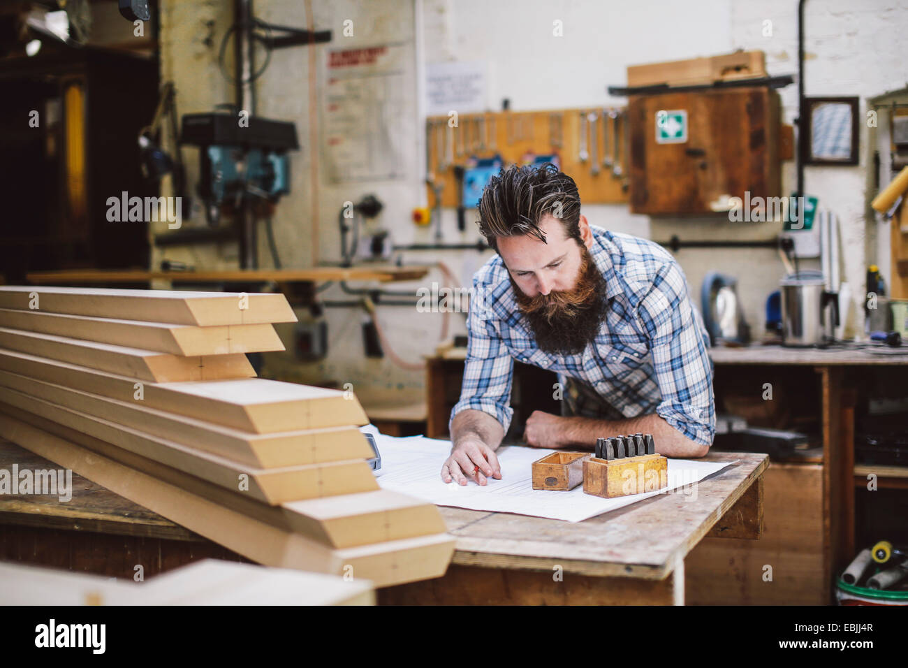Adulto medio artigiano guardando in giù a blueprint in organo workshop Foto Stock