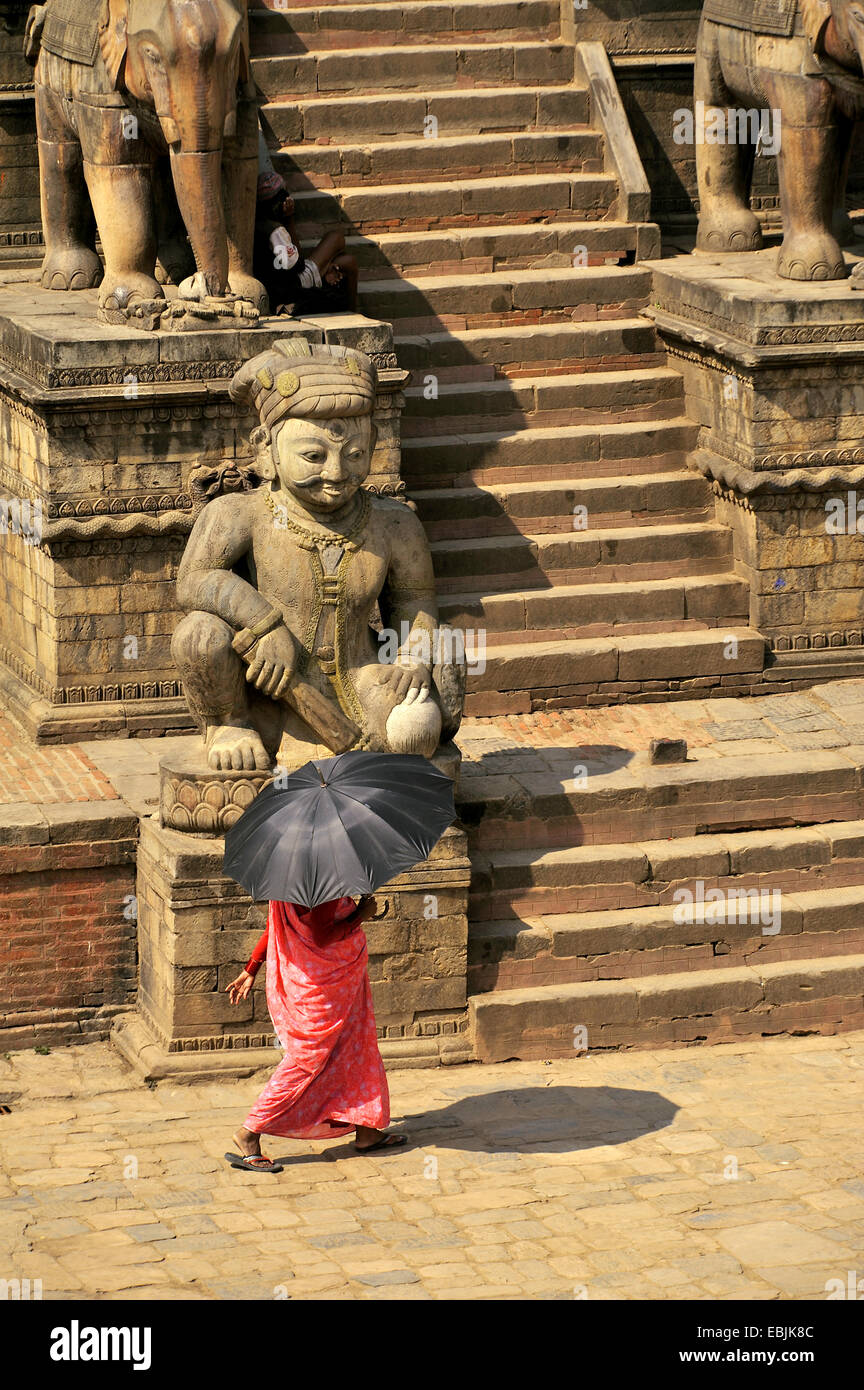 Donna con un ombrello che serve come un parasole attraversando il Bhaktapur Durbar Square presso il Royal Palace, Nepal, Bhaktapur Foto Stock