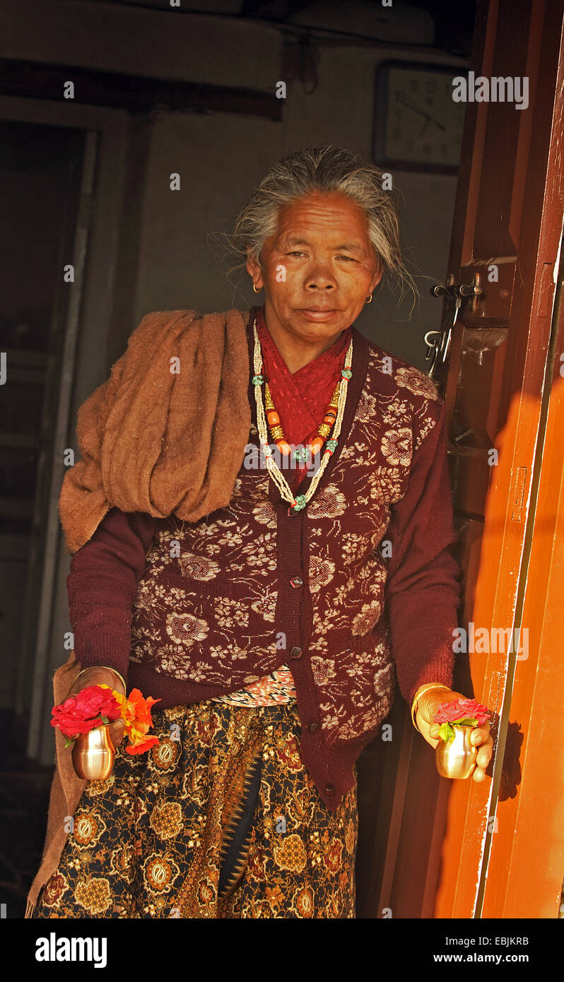 Vecchia donna dall'Annapurna Himal in piedi la porta anteriore con piccoli vasi di fiori nelle sue mani, Nepal, Annapurna Foto Stock