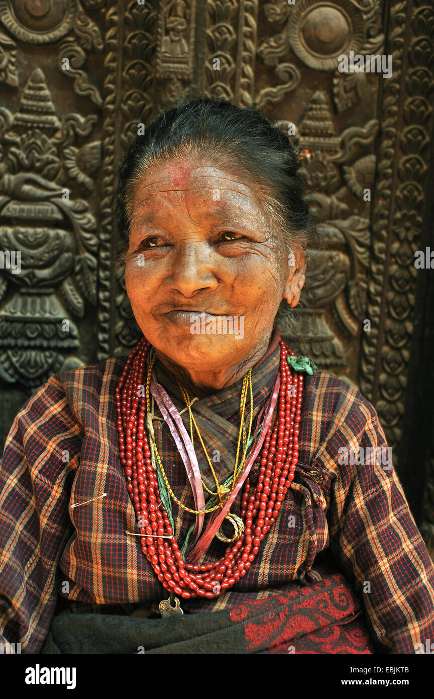 Ritratto di una vecchia donna di fronte a una porta di legno del palazzo del re ornata con sculture, Nepal, Patan Foto Stock