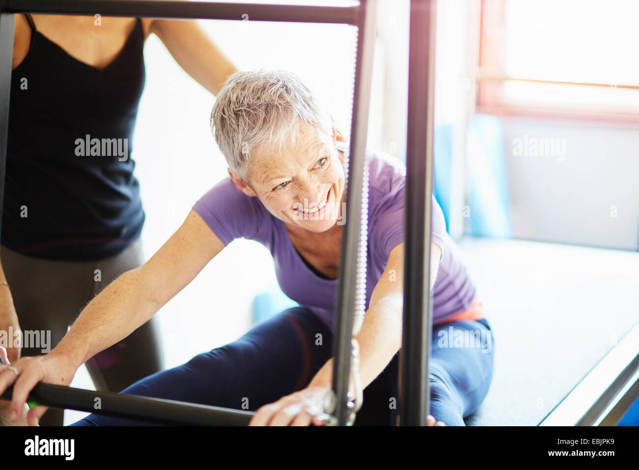 Donna matura e tutor praticare pilates sulla tabella di trapezio in palestra pilates Foto Stock
