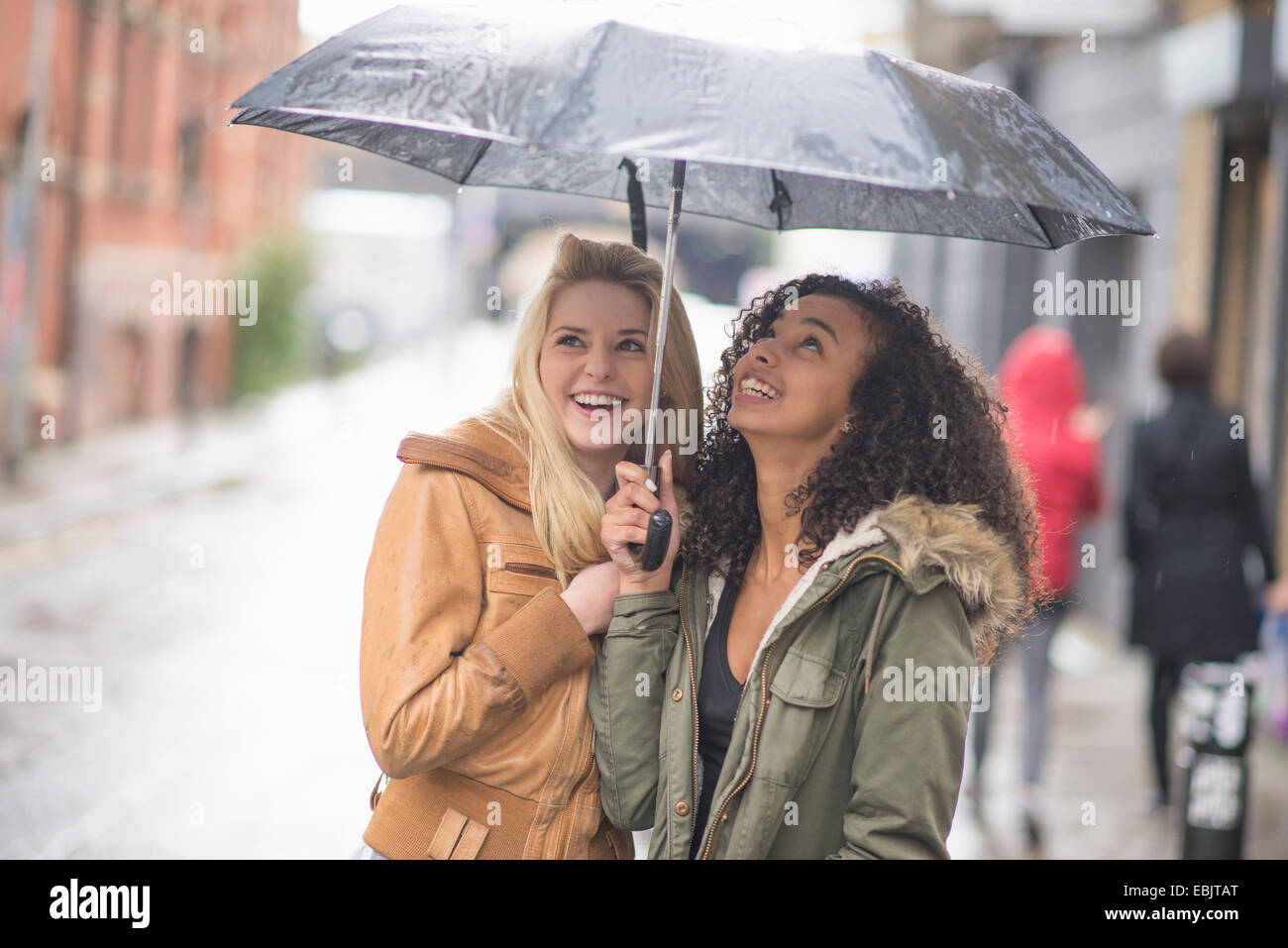 Giovani donne rifugiandosi sotto ombrellone Foto Stock