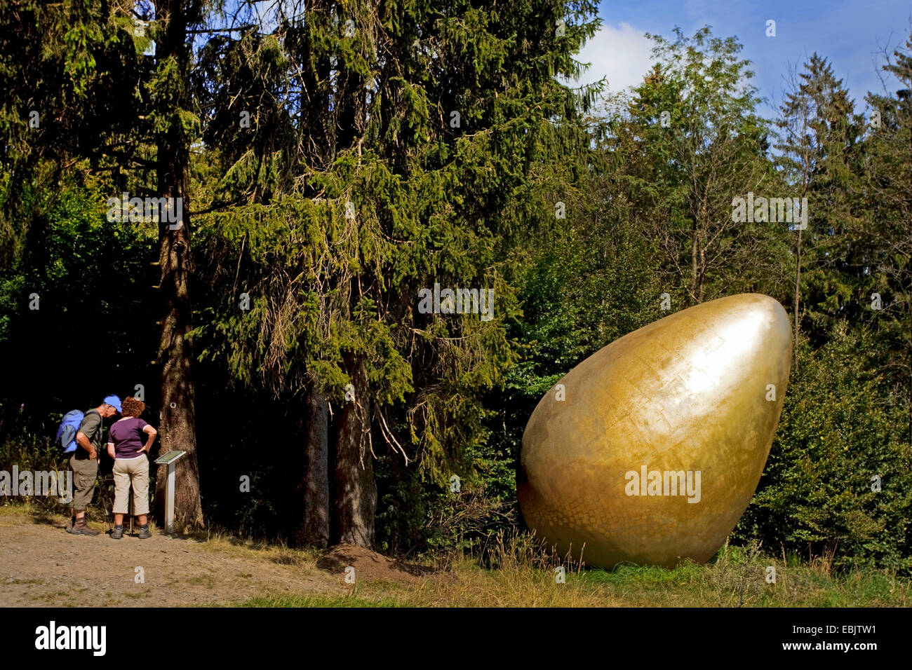 Due viandanti sul Waldskulpturenweg leggendo la targhetta con le informazioni della scultura "fu guerra zuerst?" ("Che cosa è venuto prima?") che mostra un gigante Golden Egg, in Germania, in Renania settentrionale-Vestfalia, Siegerland, Bad Berleburg Foto Stock