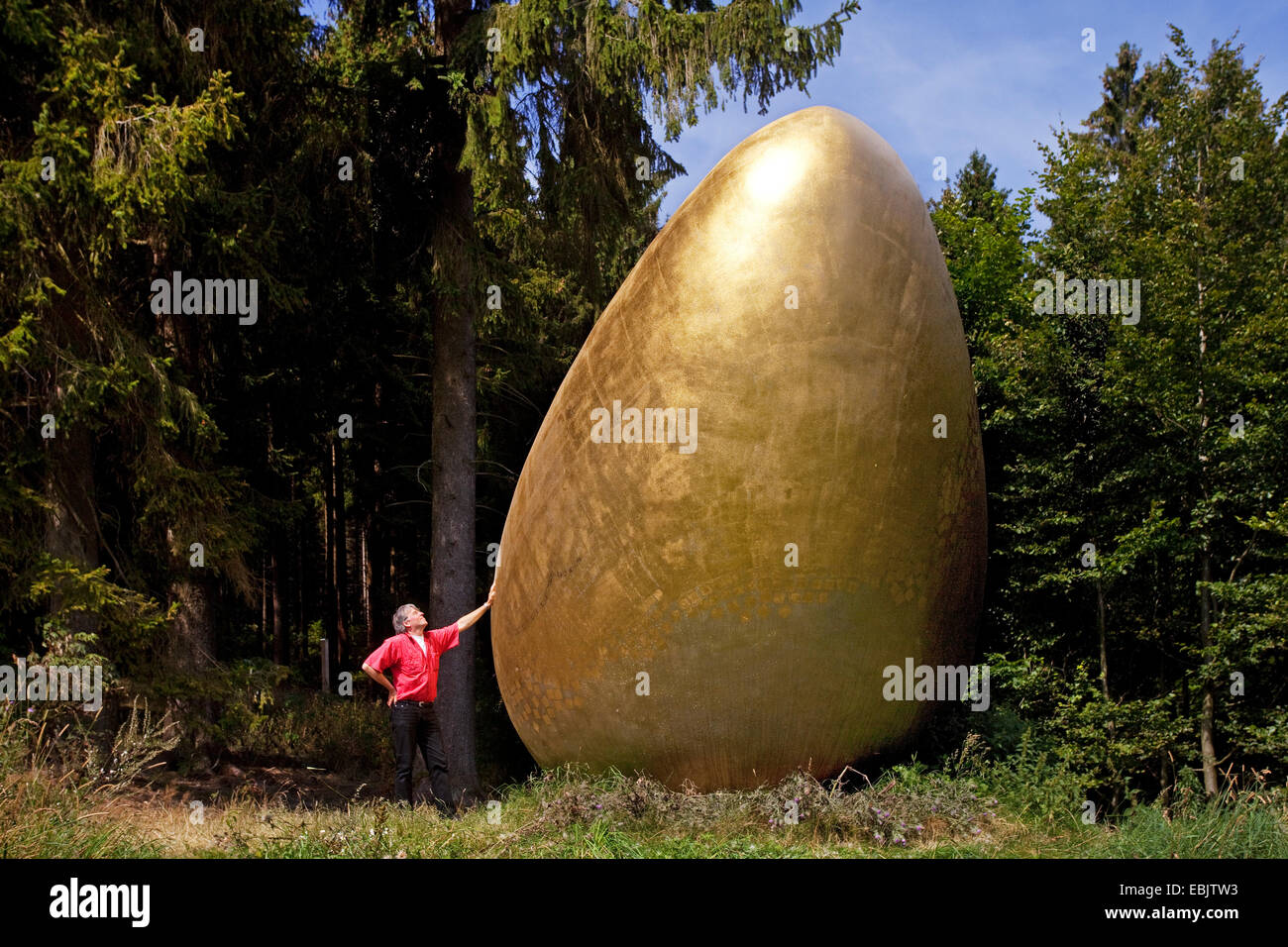 L'uomo sulla Waldskulpturenweg appoggiata contro la scultura "fu guerra zuerst?" ("Che cosa è venuto prima?") che mostra un gigante Golden Egg, in Germania, in Renania settentrionale-Vestfalia, Siegerland, Bad Berleburg Foto Stock