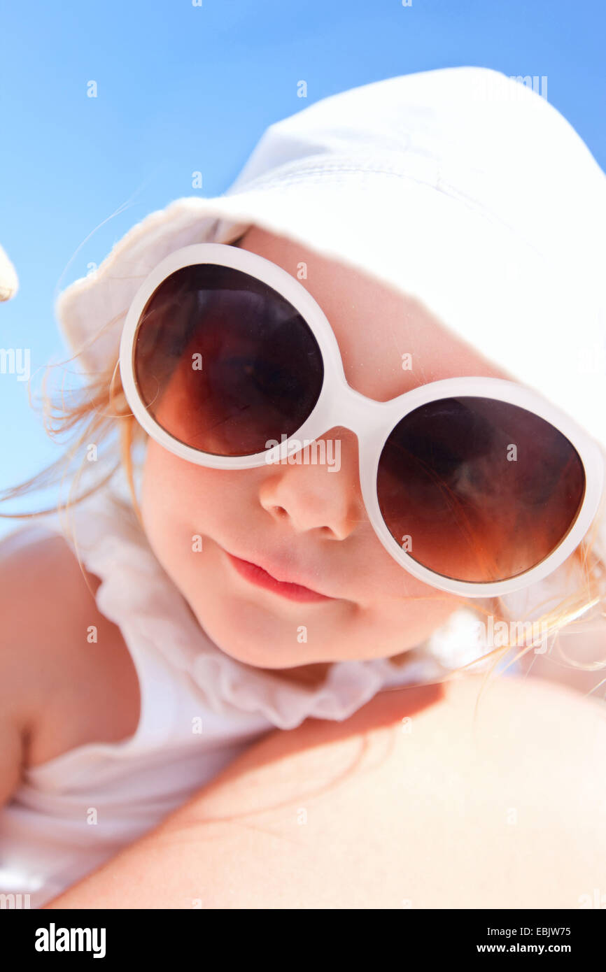 Bambina con gli occhiali da sole sul braccio di madri a sorridere per la fotocamera Foto Stock