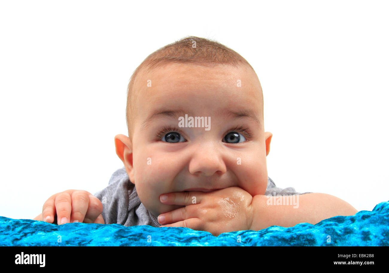 Il bambino giacente in un letto sul ventre con una mano in bocca Foto Stock