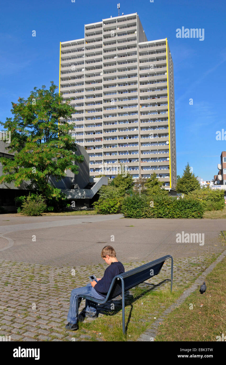 Ragazzo seduto sulla panca e riproduzione di gameboy, a torre in background, Germania, Chorweiler, Colonia Foto Stock