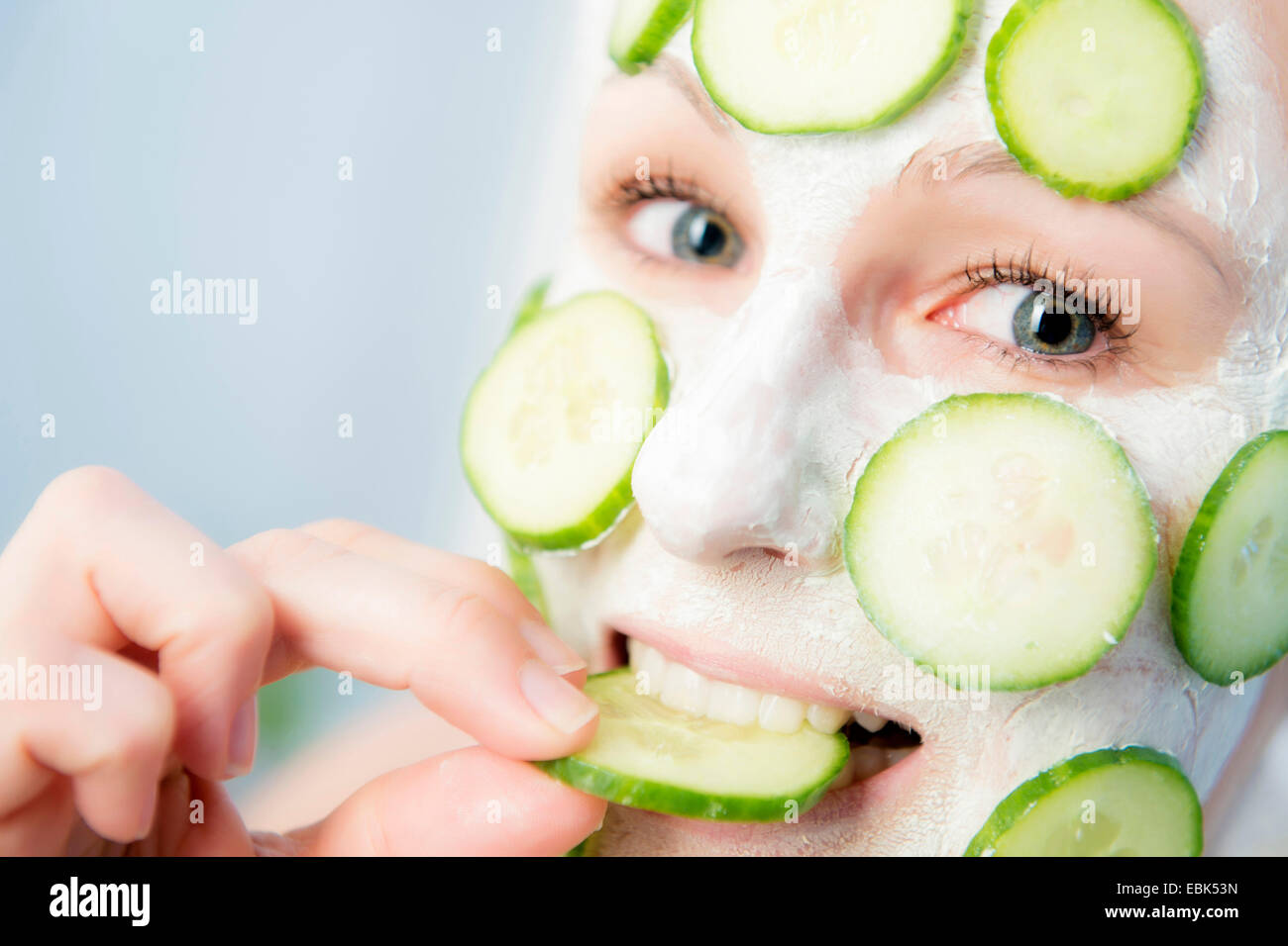 Donna con la faccia di cetriolo masque a mangiare una fetta di cetriolo Foto Stock