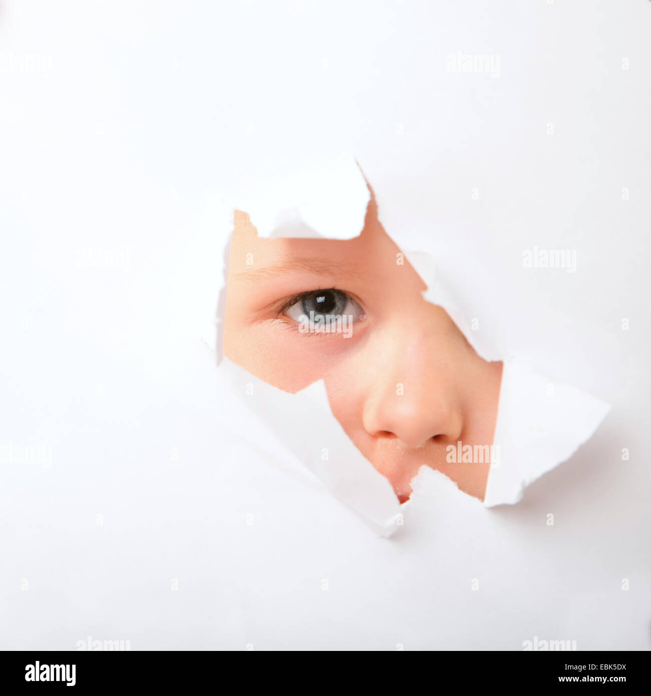Little Boy il peering attraverso il foro in un libro bianco superficie con ome eye Foto Stock