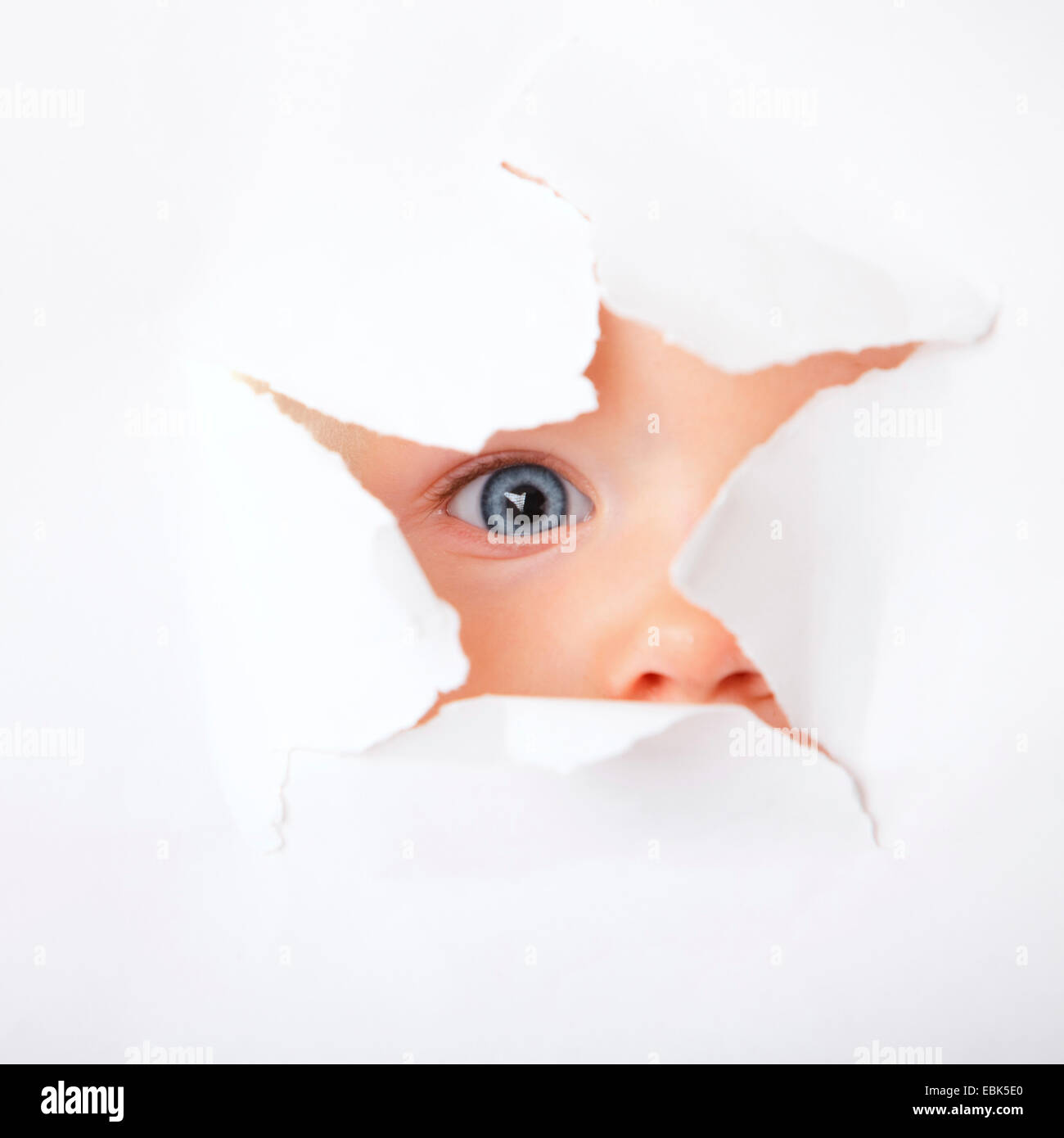 Baby il peering attraverso il foro in un libro bianco la superficie con un occhio Foto Stock