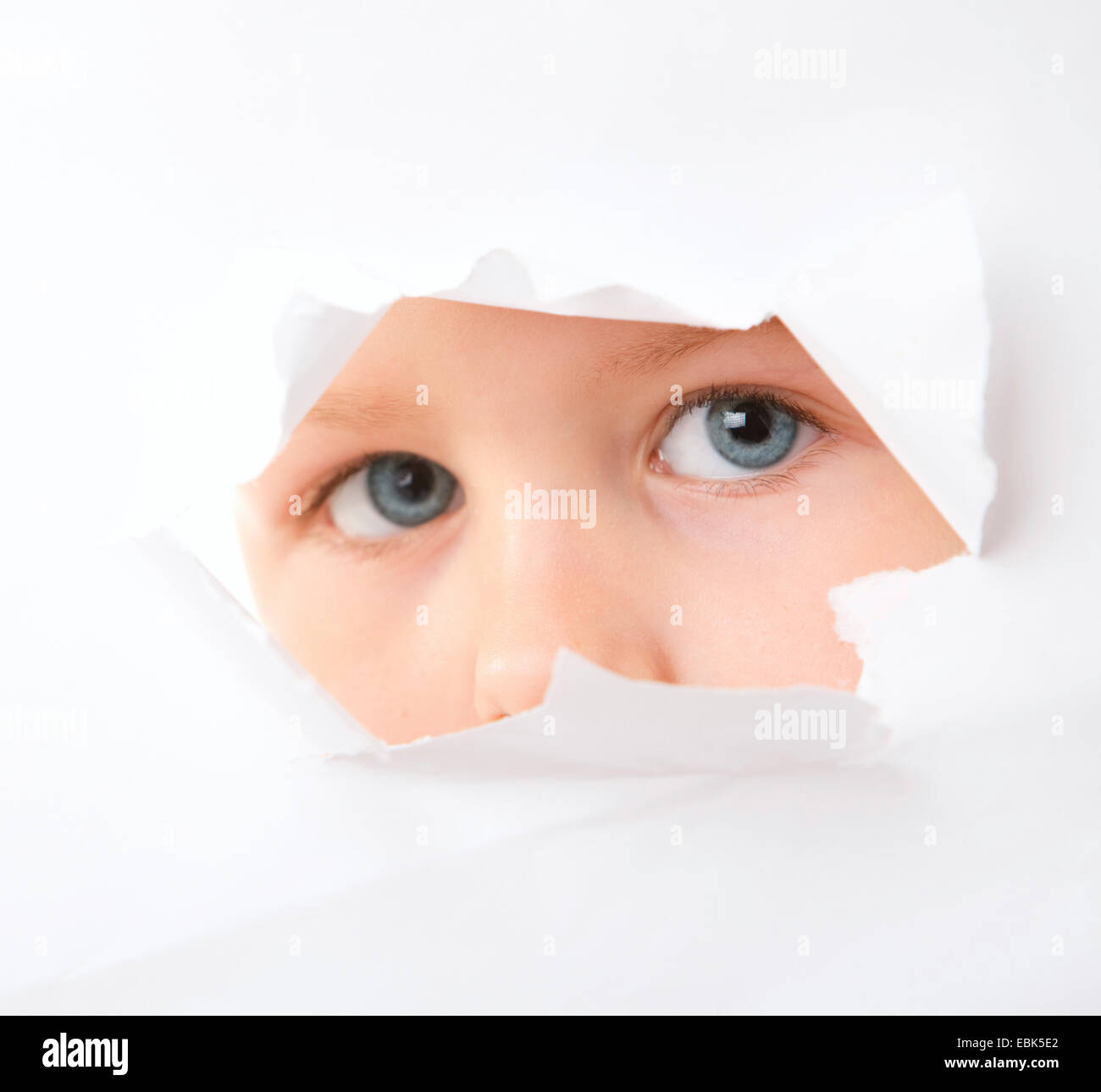Little Boy guardando attraverso il foro in un bianco la superficie della carta Foto Stock