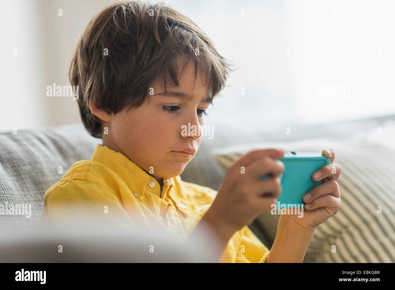 Ragazzo (6-7) seduto sul divano e utilizzando il telefono cellulare Foto Stock