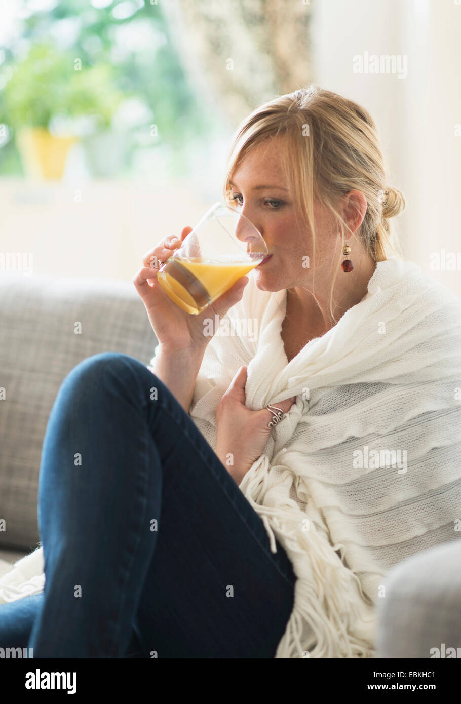 Donna seduta su un divano e bere il succo d'arancia Foto Stock