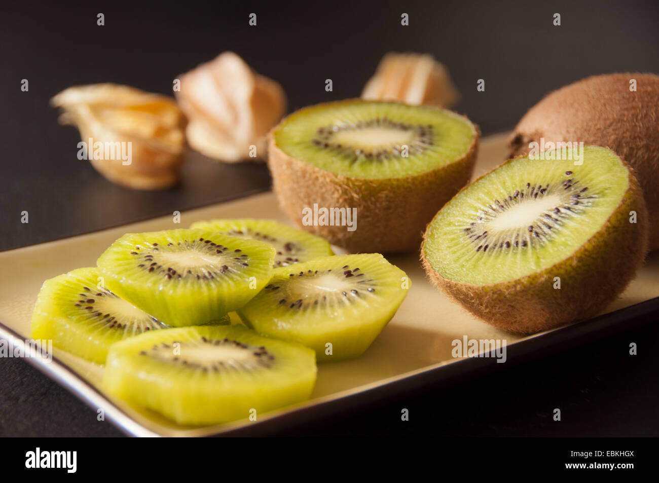 Kiwi servita in una piastra rettangolare e physalis su uno sfondo nero. (Dimezzato e fette di kiwi). Foto Stock