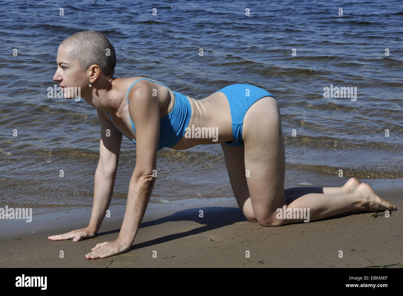Bald donna in posizione di yoga marjaryasana-bitilasana, o cat-mucca posa su una spiaggia Foto Stock
