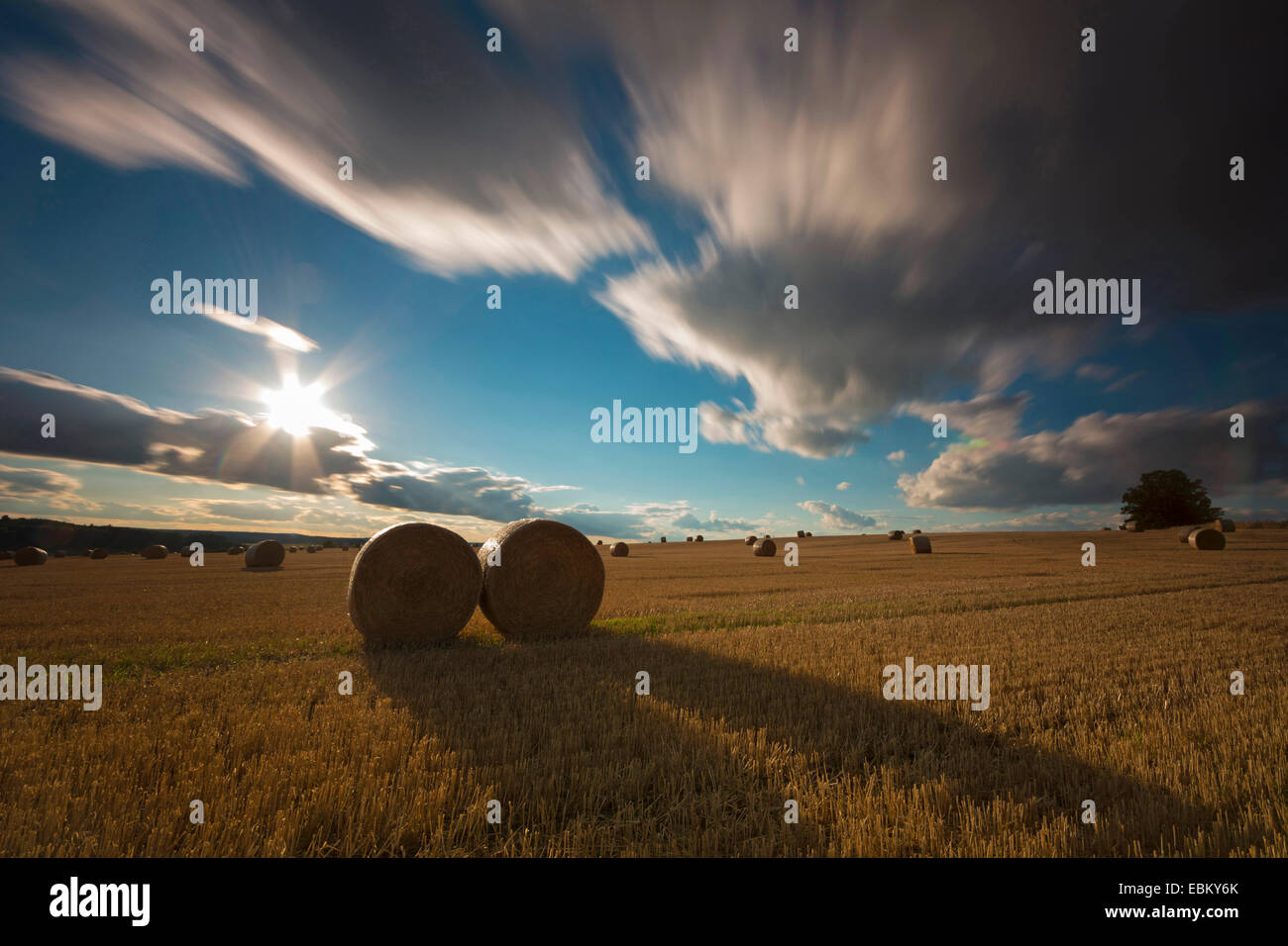 Nuvole in movimento su un campo di stoppie con balle di paglia a sunrise, longtime esposizione, Germania, Sassonia, Vogtlaendische Schweiz Foto Stock