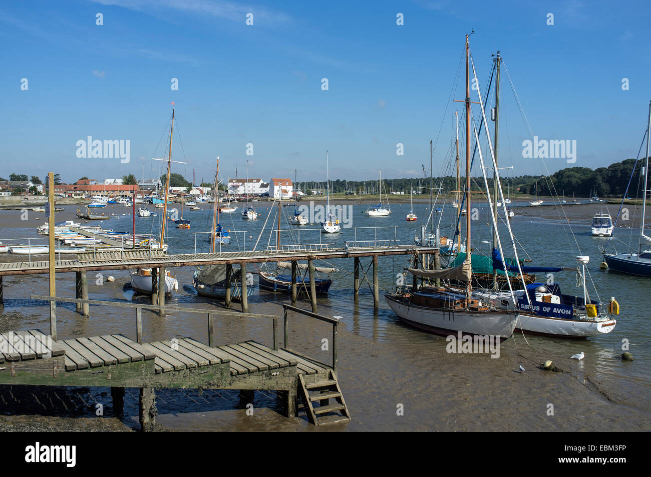 Barche ormeggiate lungo il fiume Deben a Woodbridge con mulino di marea in distanza Foto Stock