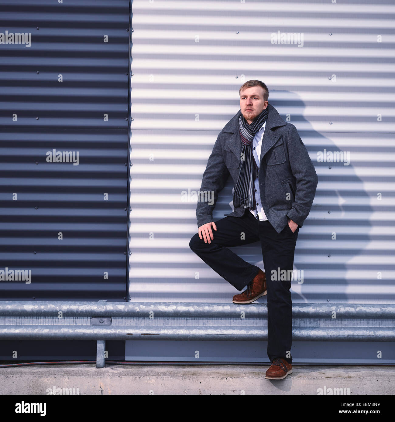 Moda giovane uomo che indossa un caldo cappotto, ferro corrugato parete su sfondo - Croce immagine elaborata Foto Stock