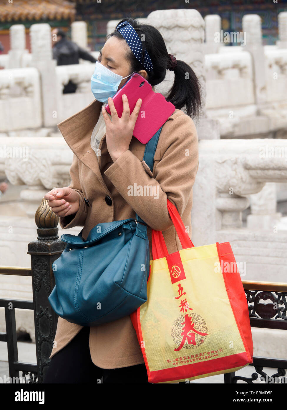 Donna cinese che usa lo smartphone mentre indossa una maschera di inquinamento a causa di smog pesante - coronavirus corona virus Foto Stock