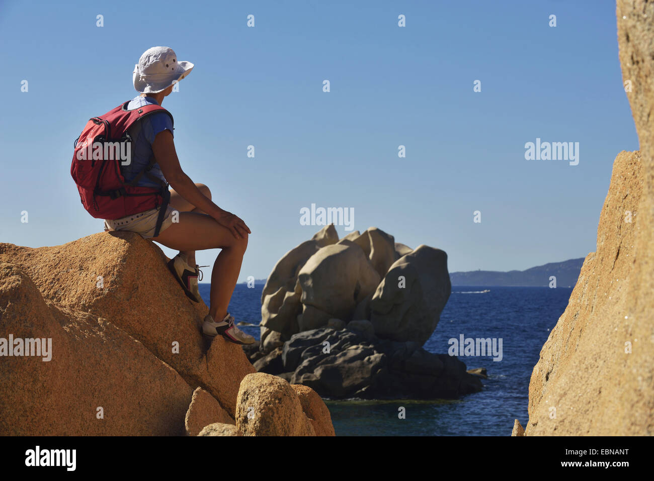 Femmina wanderer seduto su una roccia e ammirando la vista su una bizzarra formazione di roccia, Francia, Corsica Foto Stock