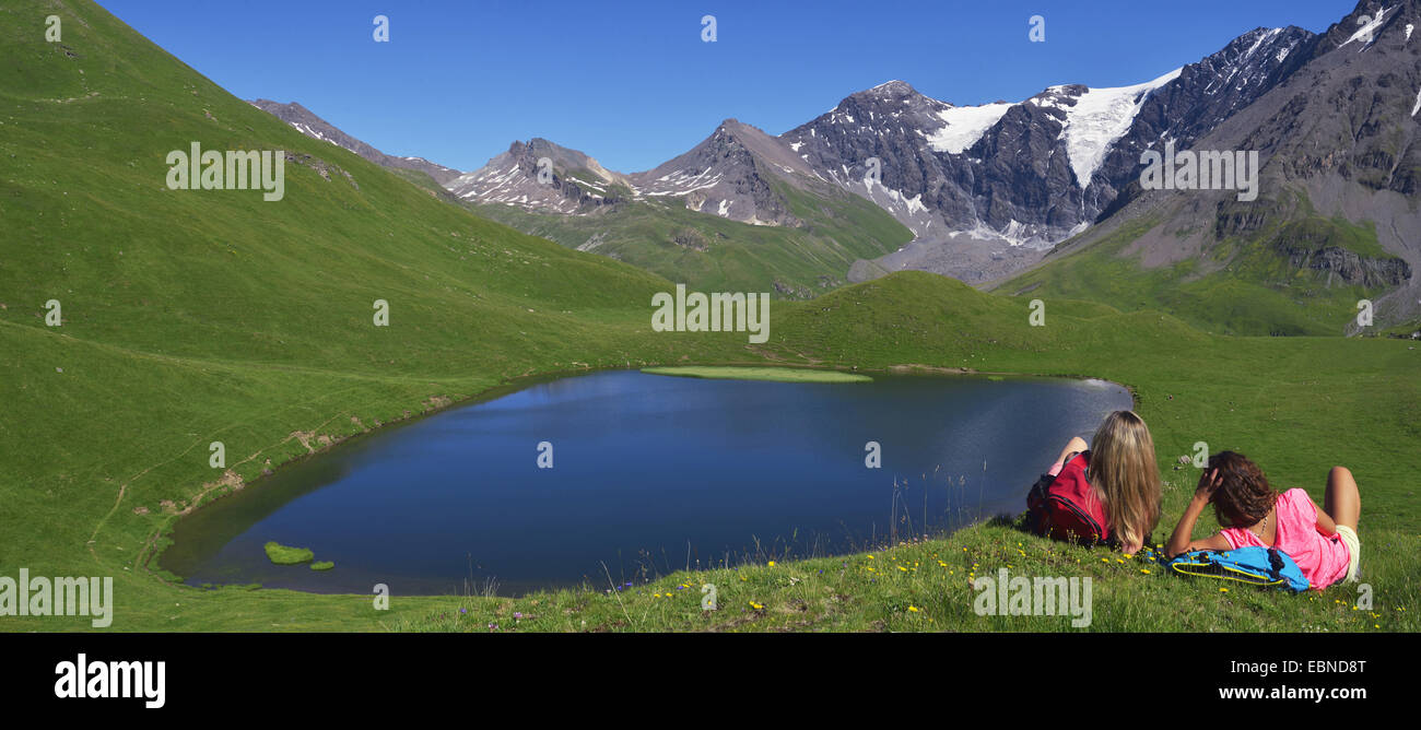 Due ragazzi seduti nel prato di montagna e godere la vista del lago di montagna, Francia, Savoie, Sainte-Foy Tarentaise Foto Stock