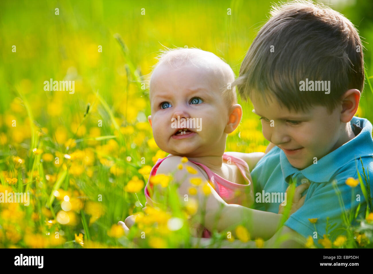 Fratello e sorella più piccola giocando in erba verde al giorno d'estate e di sole. Foto Stock