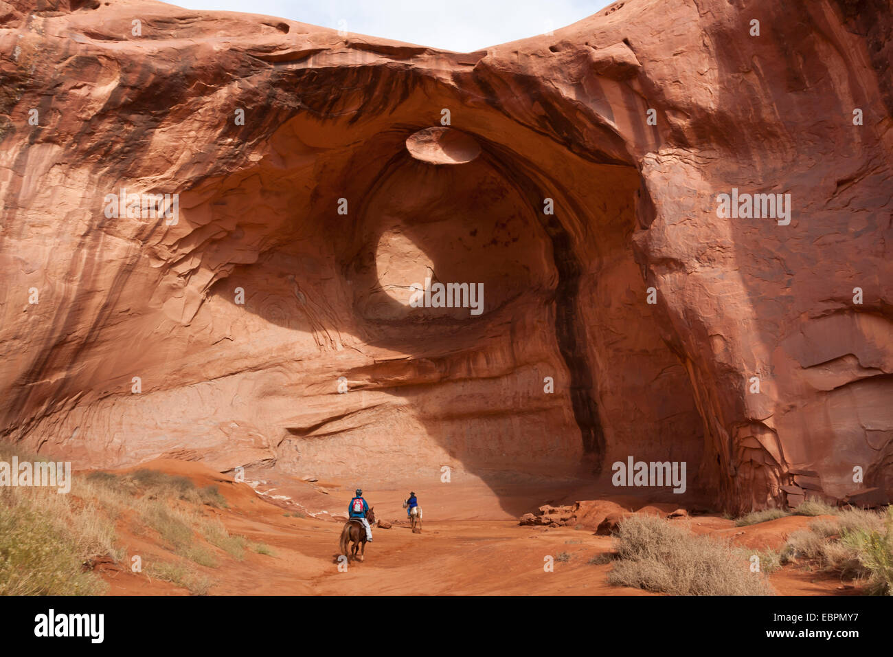 Equitazione viaggio turistico con guida Navajo passare sotto l'arco di roccia, il parco tribale Navajo Monument Valley, Utah Arizona, Stati Uniti d'America Foto Stock