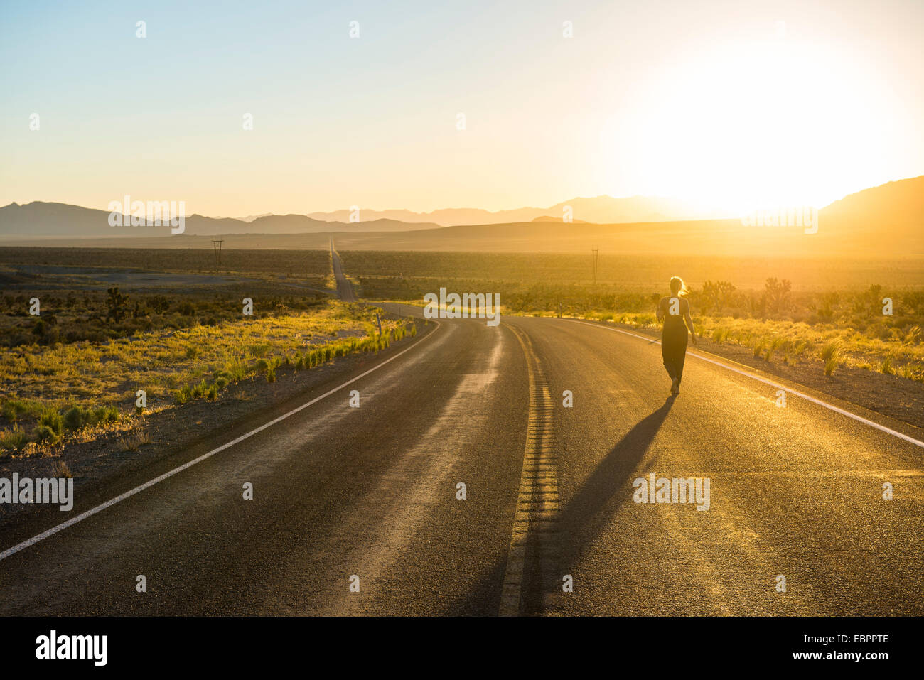 Donna che cammina verso il basso una lunga strada tortuosa al tramonto nella parte orientale del Nevada, Stati Uniti d'America, America del Nord Foto Stock