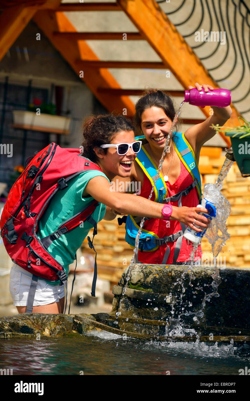 Due giovani donne escursionisti rinfrescante presso una fontana, Francia, Savoie Foto Stock