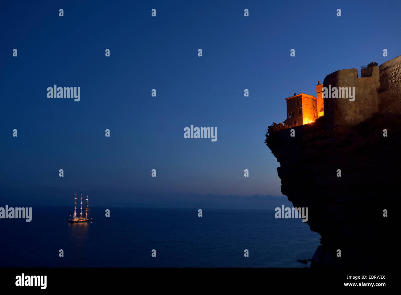 Case della città vecchia in corrispondenza del bordo di chalk cliff e illuminata di una nave a vela in luce della sera, Francia, Corsica, Bonifacio Foto Stock