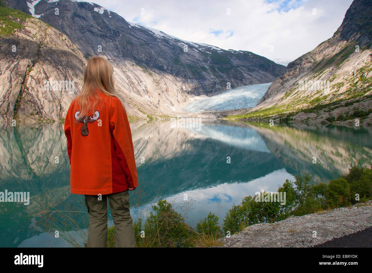 Bambino in piedi presso il lago glaciale Nigardsbrevatnet e guardando alla lingua del ghiacciaio Nigardsbreen, Norvegia, Jostedalsbreen National Park, Jostetal Foto Stock