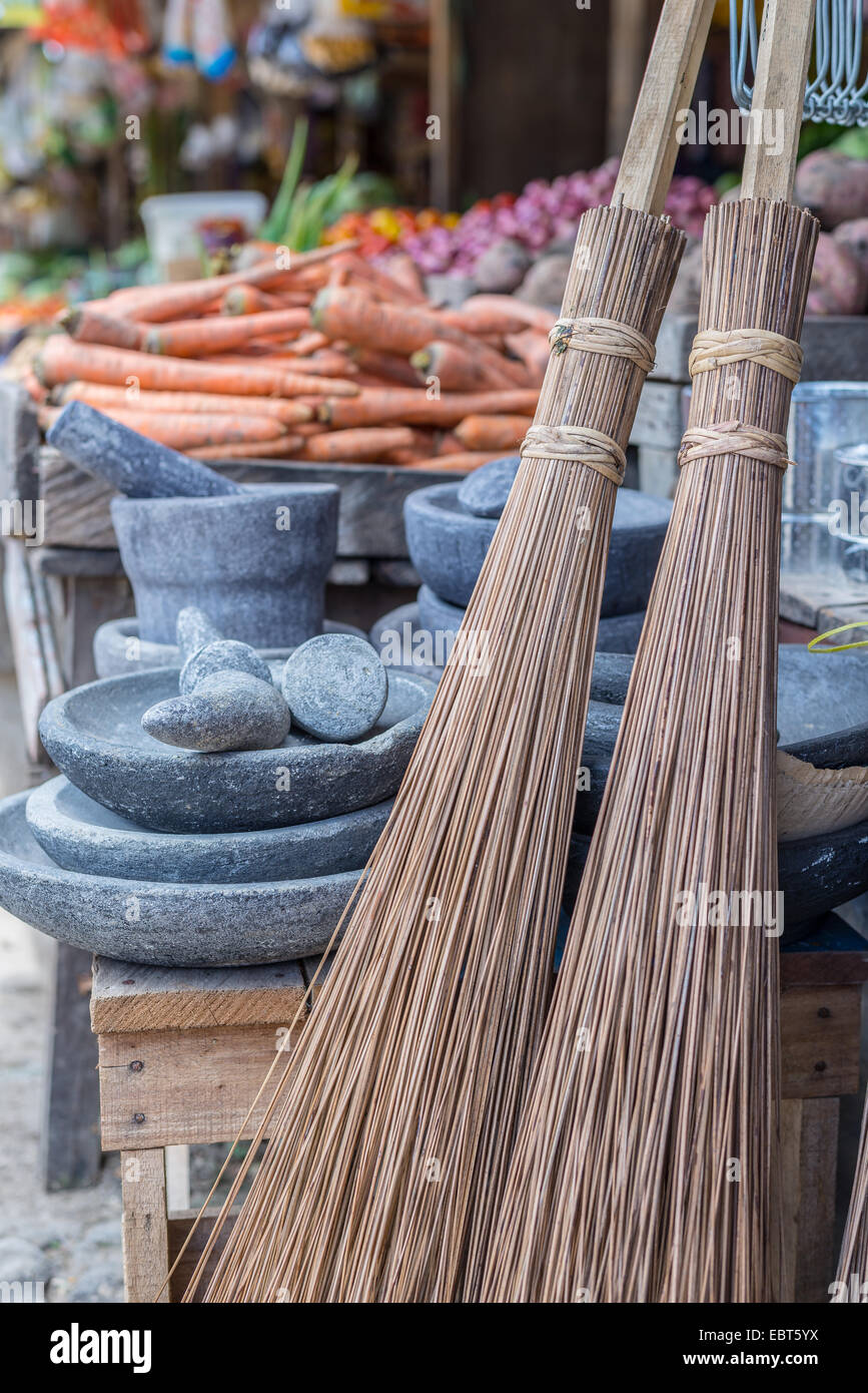 Messa a fuoco selettiva sul gruppo di vecchio stile scope di paglia per vendere nel mercato asiatico. Mortai di pietra e le verdure in background. Foto Stock