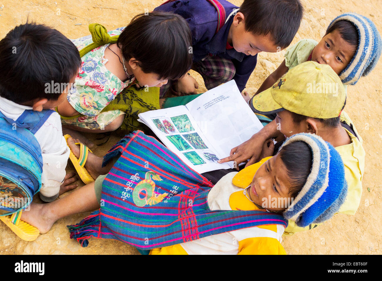 Un gruppo di bambini della scuola di leggere un libro con le foto al di fuori della loro scuola in Birmania, Myanmar, sud-est asiatico Foto Stock