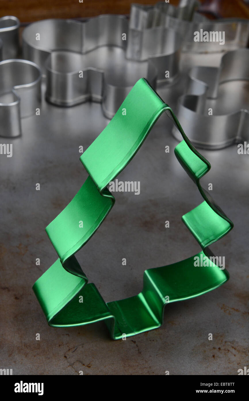 Primo piano di un metallo verde albero di Natale cookie cutter su una teglia da forno con frese casuale in background. Foto Stock