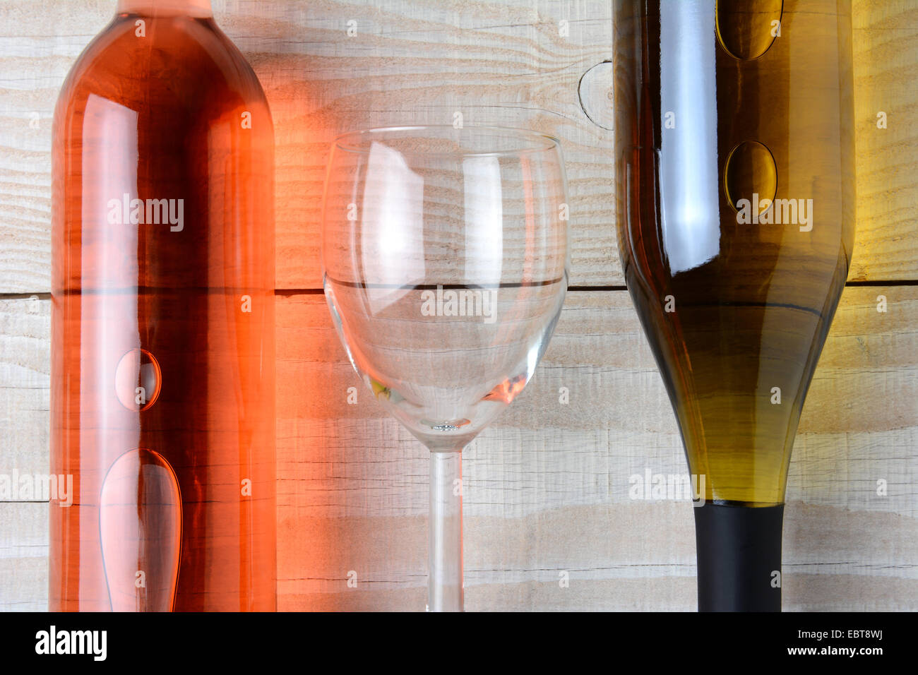 Primo piano di un bicchiere di vino tra una bottiglia di vino rosso e una bottiglia di vino bianco. Tutti e tre gli oggetti sono la posa su un bianco rustico Foto Stock