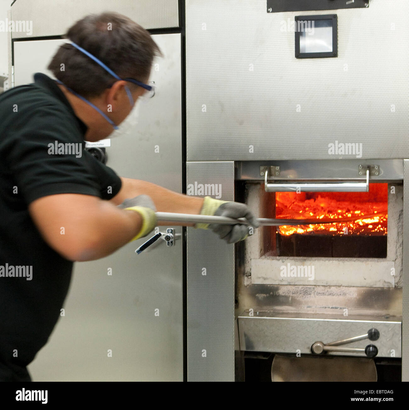 Membro del personale di un crematorio di agitazione è il fuoco nel forno Foto Stock