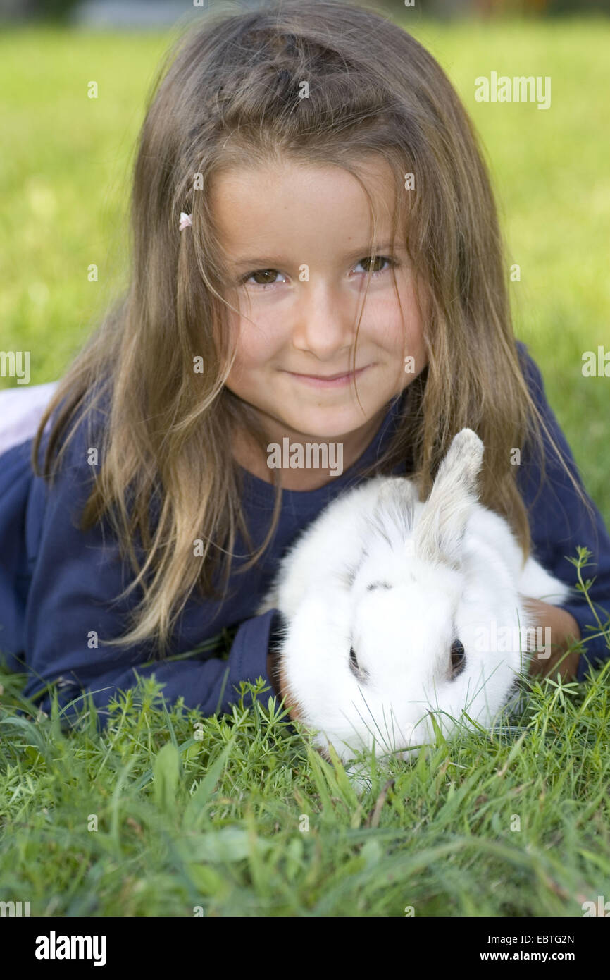 Bambina giacente in un prato e tenendo un coniglio domestico nelle sue mani Foto Stock