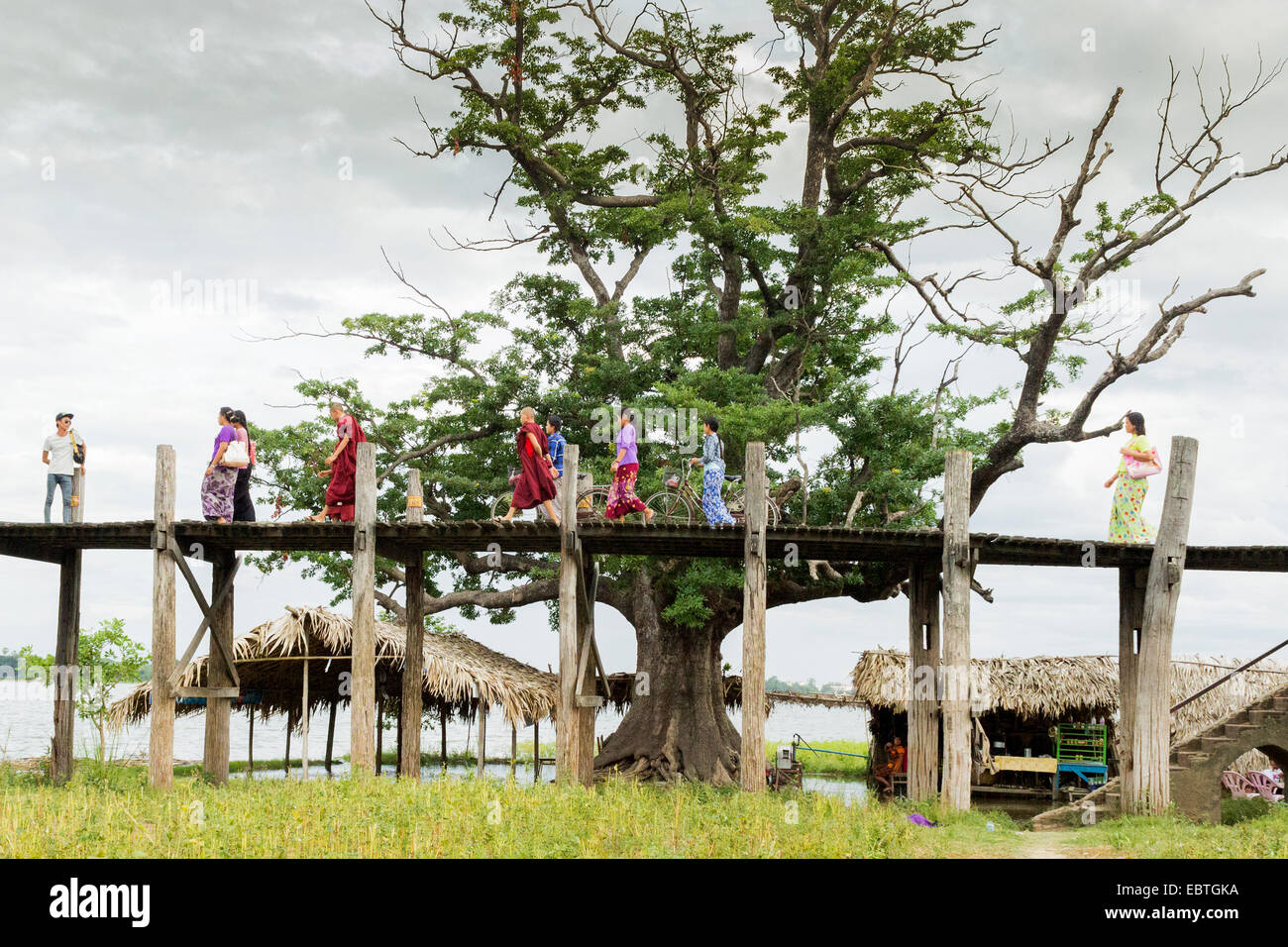 Popolo birmano indossando abiti tradizionali attraversano il lago Taungthaman sulla U Bein Bridge, Amarapura, Mandalay Birmania Foto Stock
