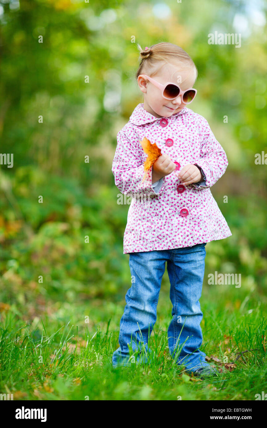 Carino bambina in un parco in possesso di una foglia di autunno Foto Stock