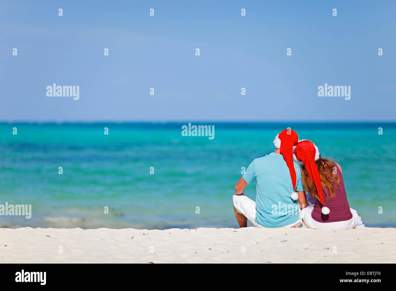 Un giovane in amore seduta con cappelli di Babbo Natale a Sandy Beach Foto Stock
