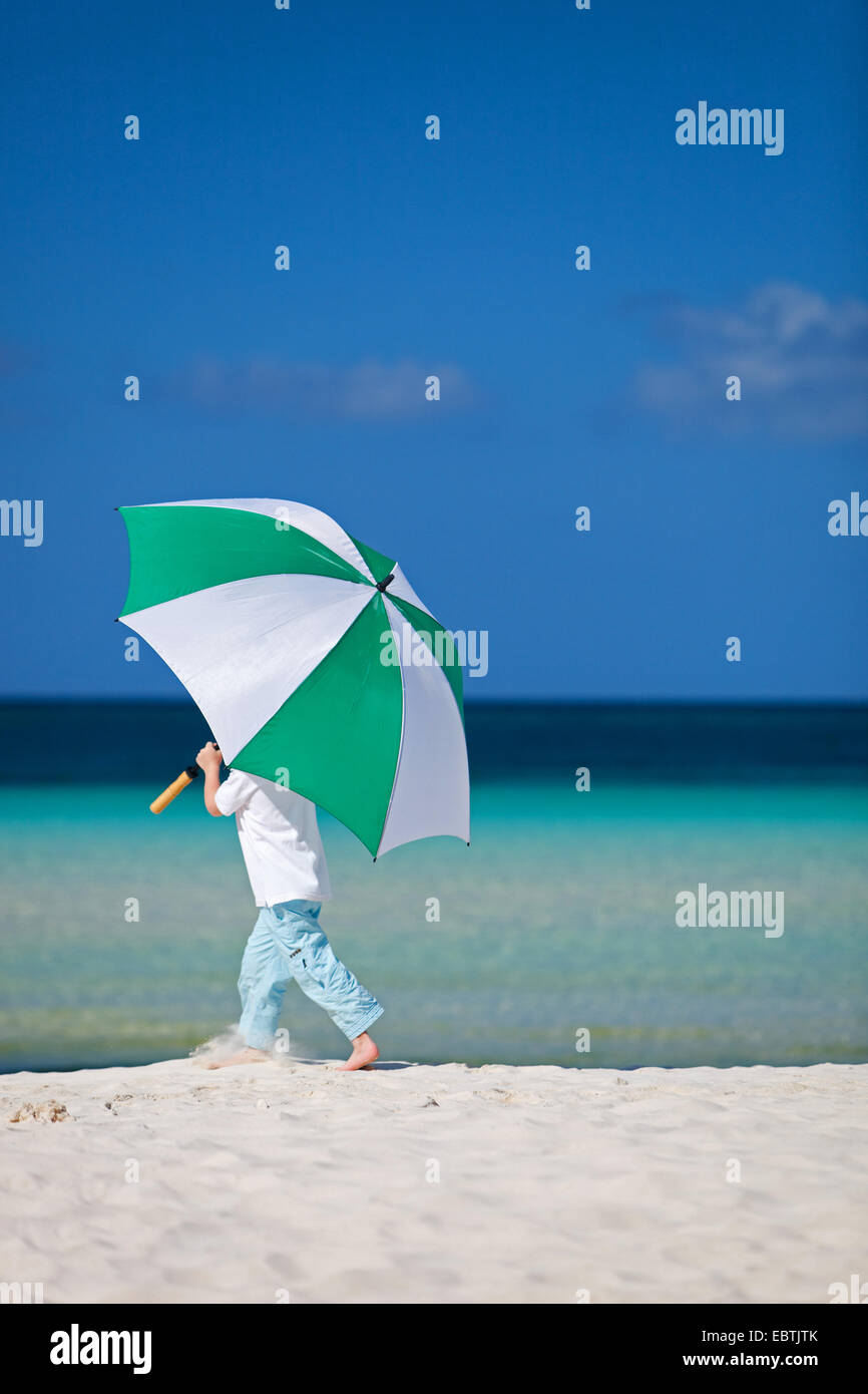 Little Boy con ombrellone a camminare sulla spiaggia di sabbia Foto Stock