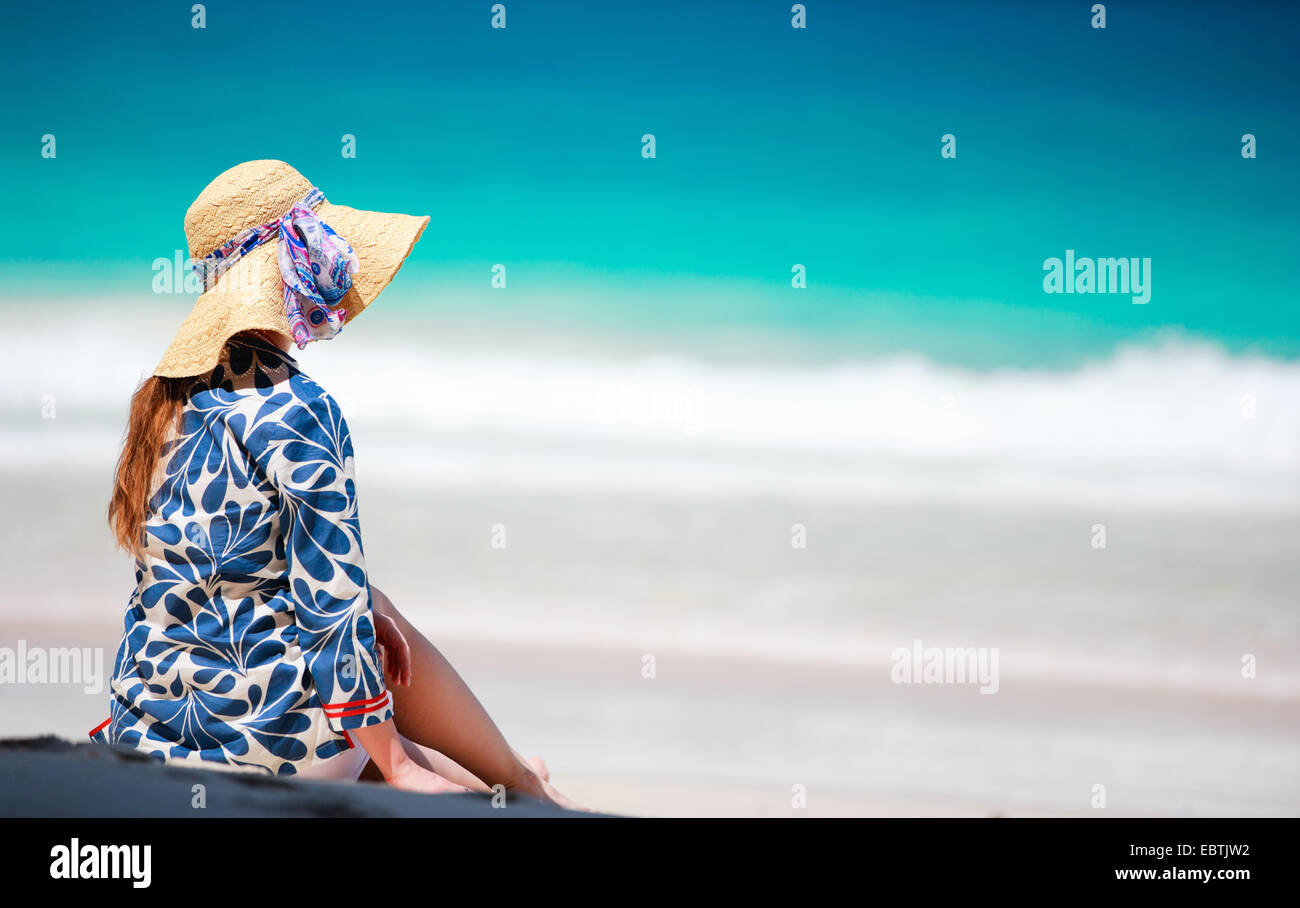 Donna con cappello per il sole seduto sulla spiaggia sabbiosa, vista posteriore Foto Stock