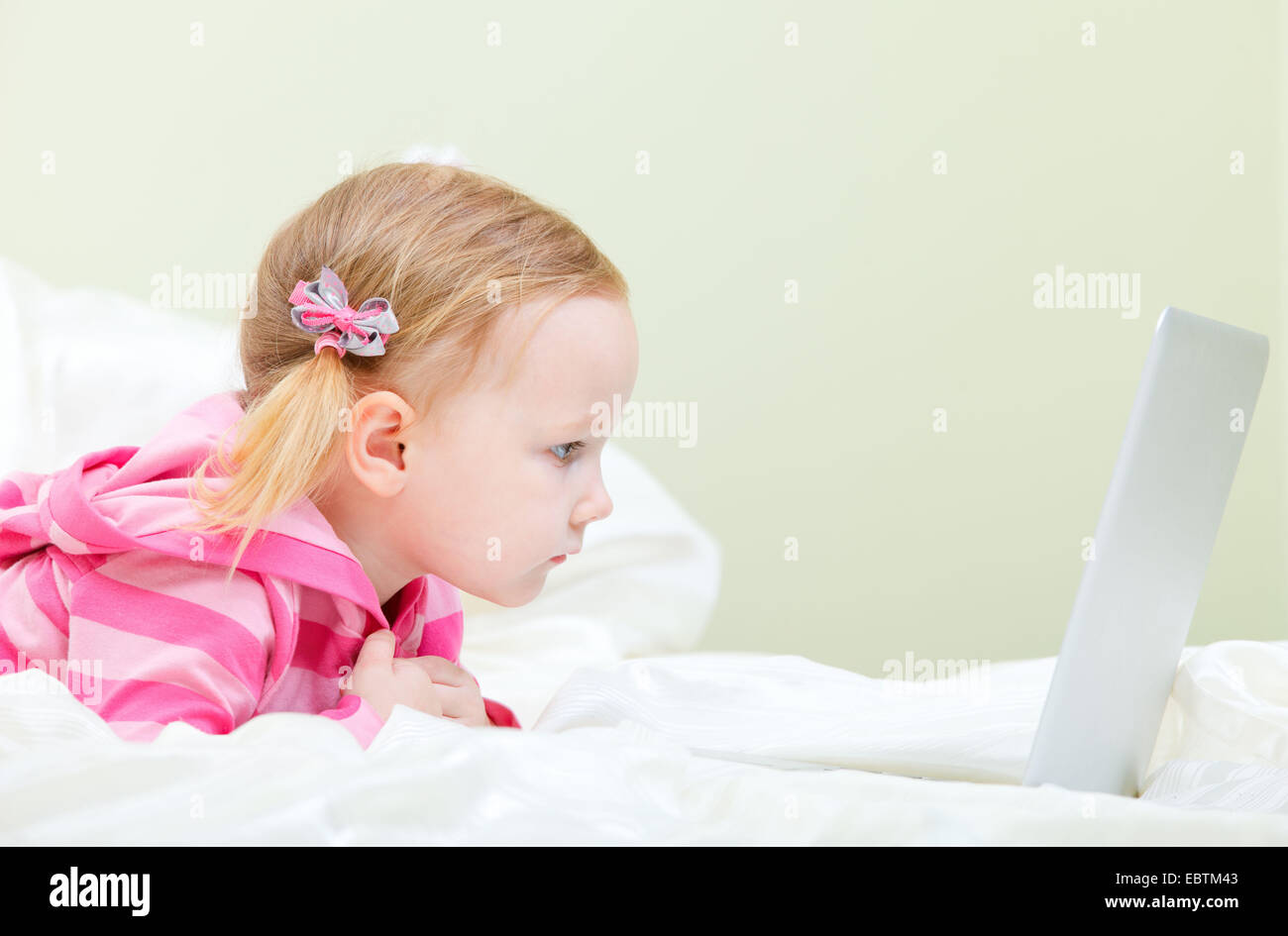 Bambina che giace nel letto di fronte a un computer portatile Foto Stock