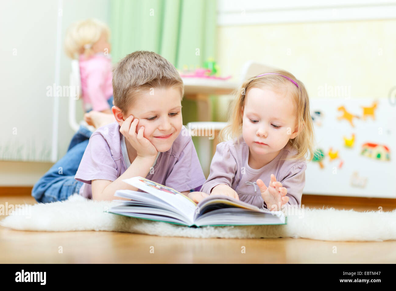 Fratello e Sorella sdraiato sul pavimento nel loro nido la lettura di un libro insieme Foto Stock