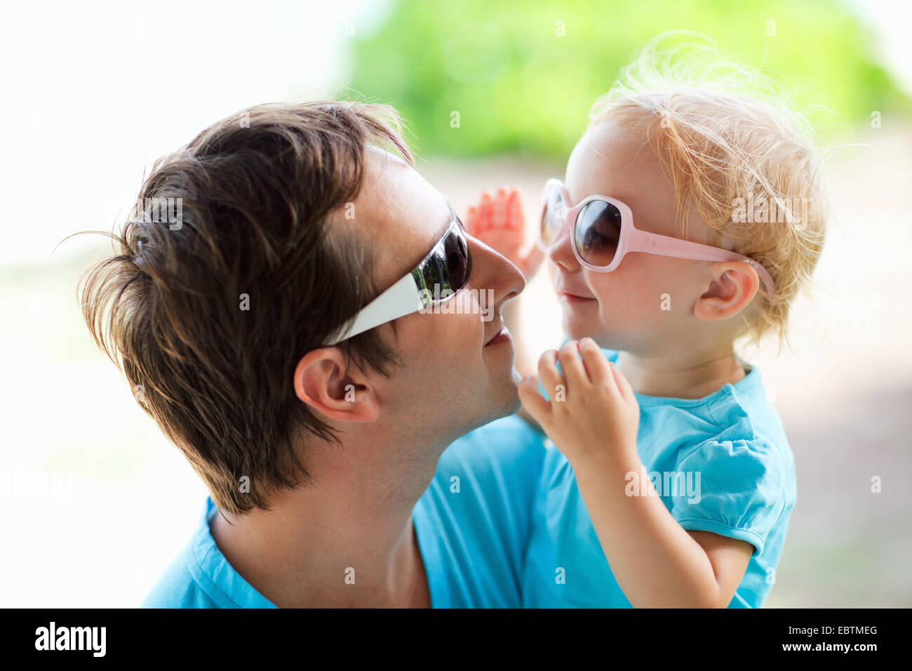 Giovane padre e figlia piccola sul suo braccio felicemente che ognuno guarda negli occhi dell'altro attraverso i loro occhiali da sole Foto Stock