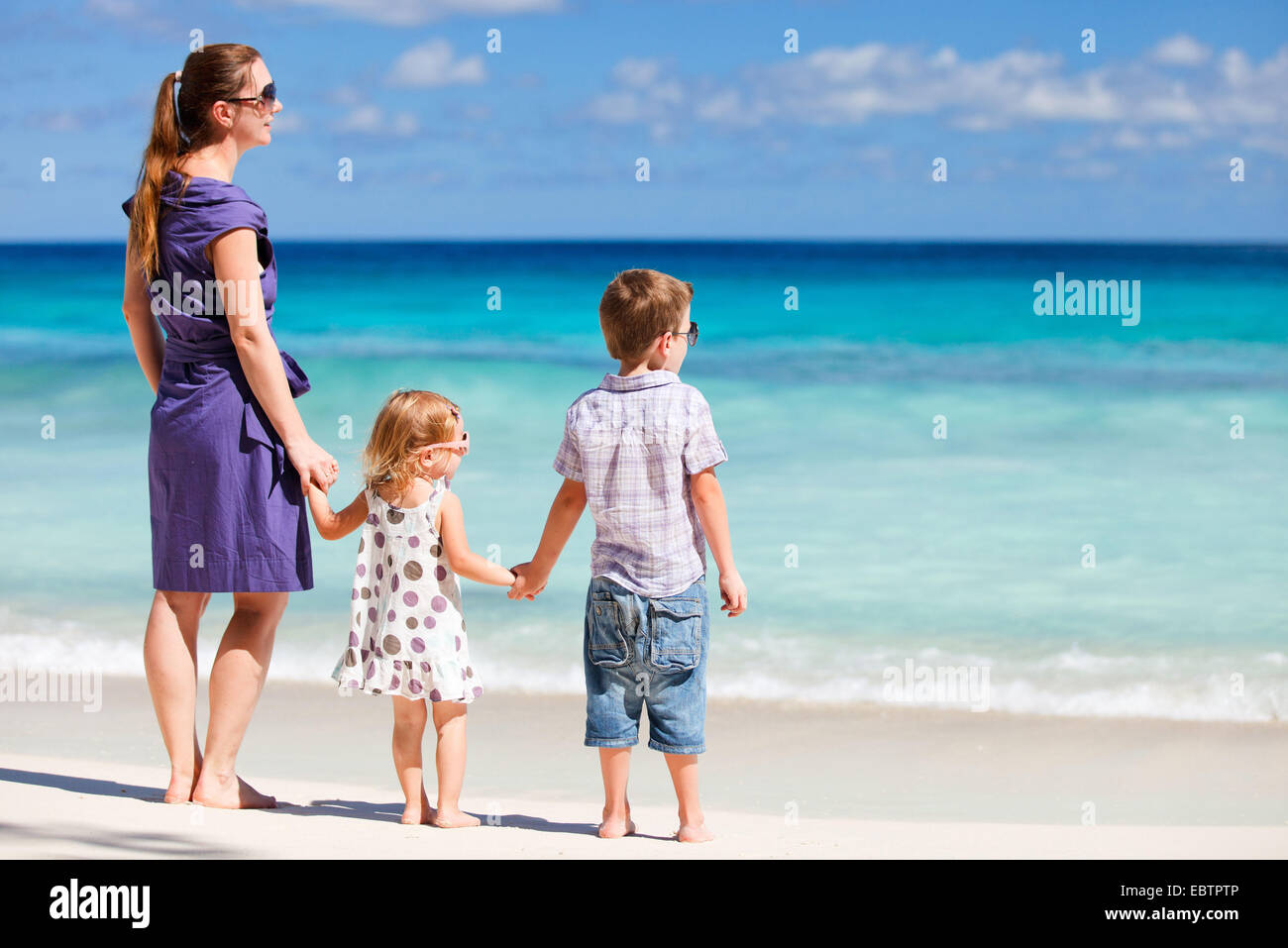Madre di due bambini in piedi sulla spiaggia tropicale Foto Stock