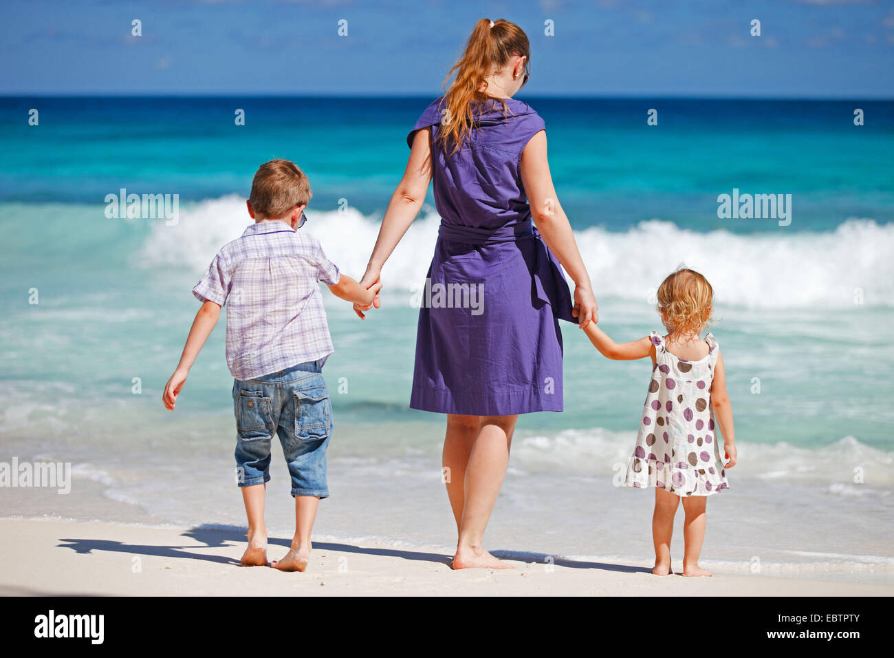 Madre di due bambini passeggiate sulla spiaggia tropicale Foto Stock